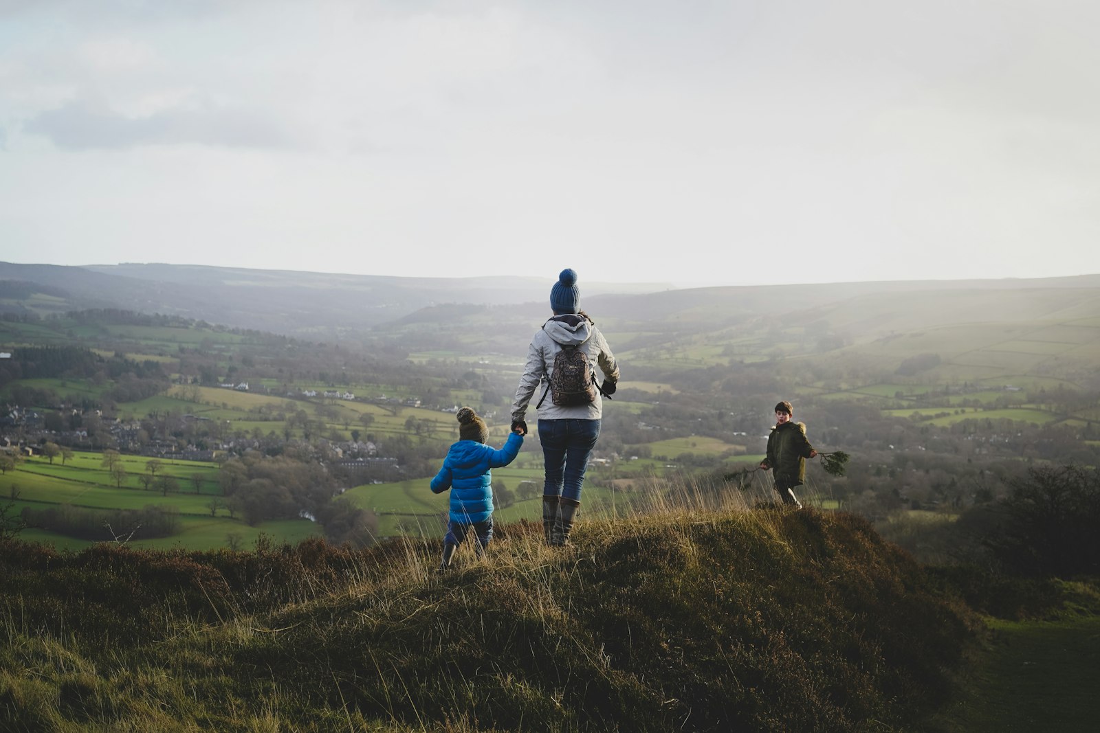 Mutter mit zwei Kindern beim Wandern durch grüne Hügel in der Natur